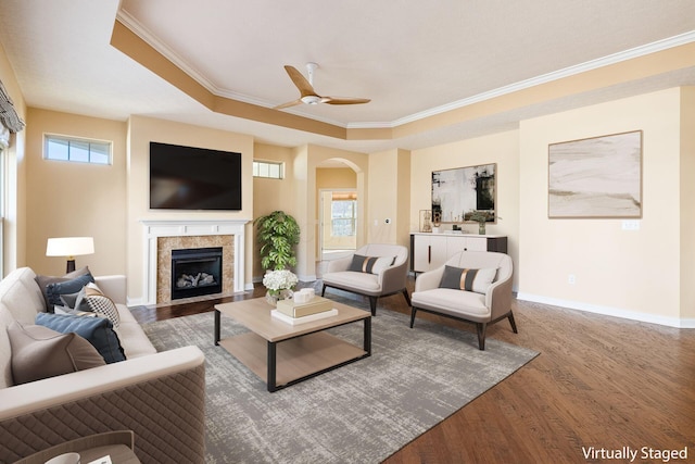 living room featuring ceiling fan, crown molding, a tray ceiling, a tiled fireplace, and hardwood / wood-style flooring