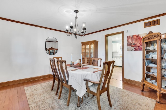 dining area featuring light wood-type flooring, crown molding, and an inviting chandelier