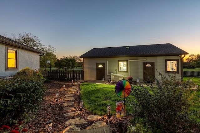 back house at dusk featuring a lawn