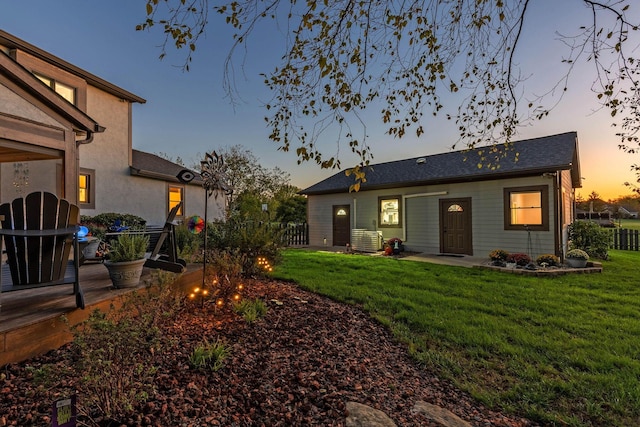 back house at dusk featuring central AC unit and a lawn