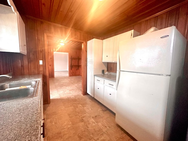 kitchen with wood ceiling, sink, white refrigerator, white cabinetry, and wood walls