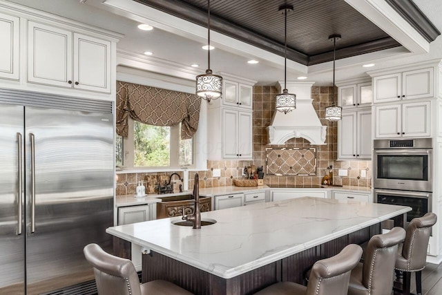 kitchen featuring hanging light fixtures, light stone counters, a breakfast bar, a center island with sink, and appliances with stainless steel finishes