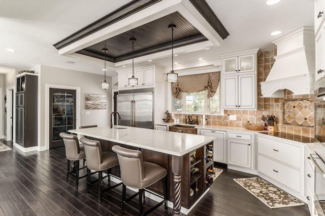 kitchen featuring a raised ceiling, decorative light fixtures, a center island with sink, dark hardwood / wood-style floors, and built in refrigerator