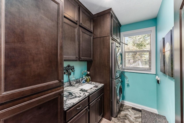 washroom with a textured ceiling, stacked washer / drying machine, and sink