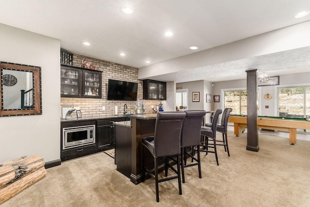 bar with stainless steel microwave, light stone counters, light colored carpet, a textured ceiling, and pool table