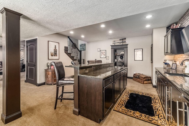 kitchen featuring sink, light colored carpet, a textured ceiling, a breakfast bar area, and dark brown cabinets