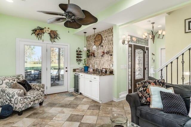 interior space featuring white cabinetry, beverage cooler, hanging light fixtures, dark stone counters, and ceiling fan with notable chandelier