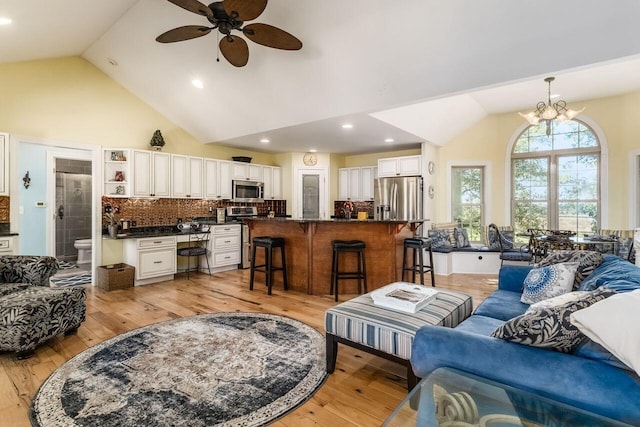 living room featuring ceiling fan with notable chandelier, vaulted ceiling, and light hardwood / wood-style flooring