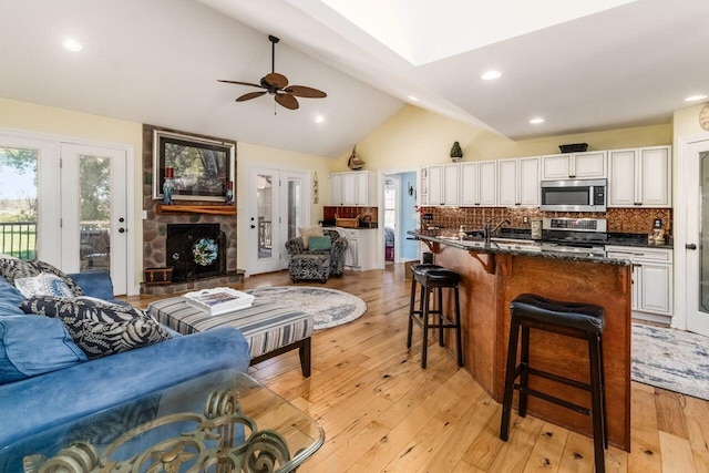 living room with lofted ceiling with skylight, sink, ceiling fan, light wood-type flooring, and a fireplace