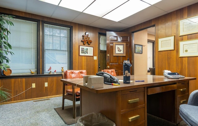 carpeted office with a paneled ceiling, wood walls, and built in desk