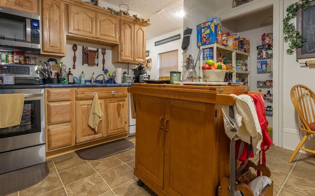 kitchen featuring a textured ceiling, dark tile patterned floors, and stainless steel appliances