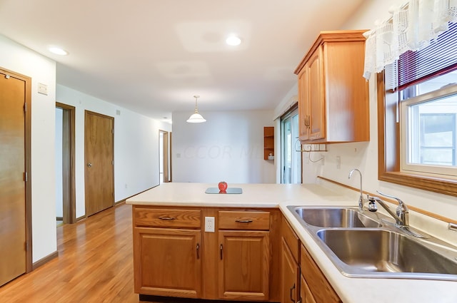 kitchen with kitchen peninsula, sink, pendant lighting, and light wood-type flooring