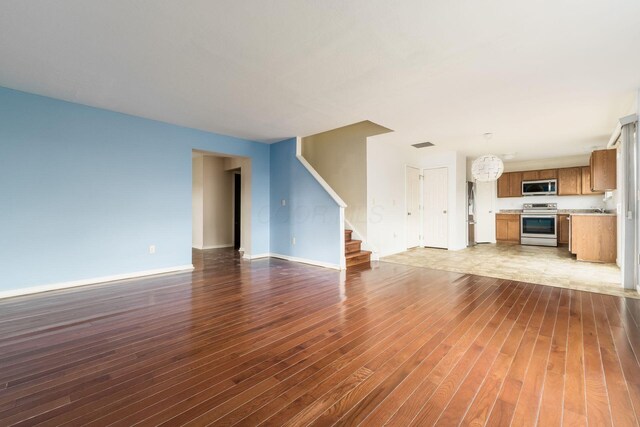 unfurnished living room featuring stairs, baseboards, dark wood-type flooring, and visible vents