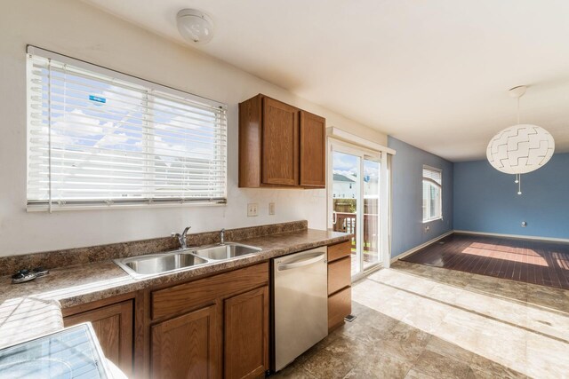 kitchen with stainless steel dishwasher, brown cabinetry, hanging light fixtures, a sink, and dark countertops