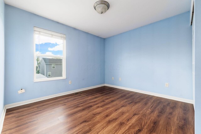 unfurnished room featuring baseboards, dark wood finished floors, and visible vents