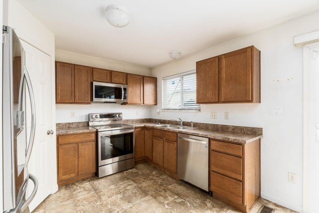 kitchen with a sink, brown cabinets, dark countertops, and appliances with stainless steel finishes