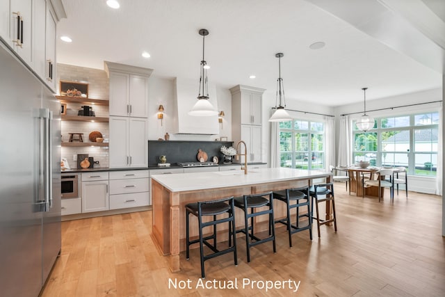 kitchen featuring stainless steel appliances, an island with sink, sink, and decorative light fixtures