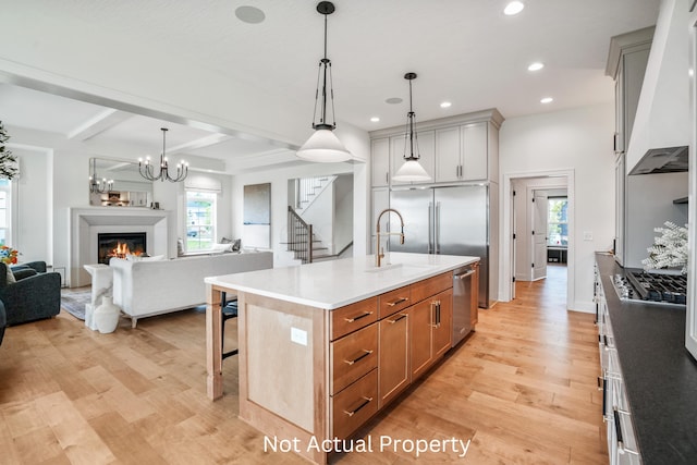 kitchen featuring premium range hood, appliances with stainless steel finishes, a breakfast bar, decorative light fixtures, and an island with sink