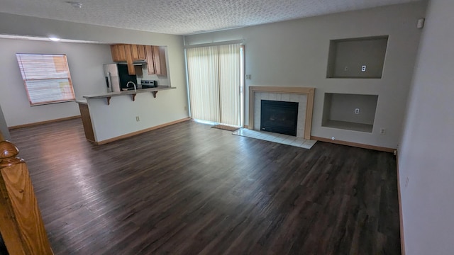 unfurnished living room featuring dark wood-type flooring, a tile fireplace, and a textured ceiling