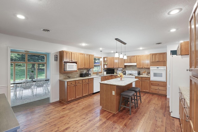 kitchen featuring white appliances, decorative light fixtures, a breakfast bar, a kitchen island, and sink