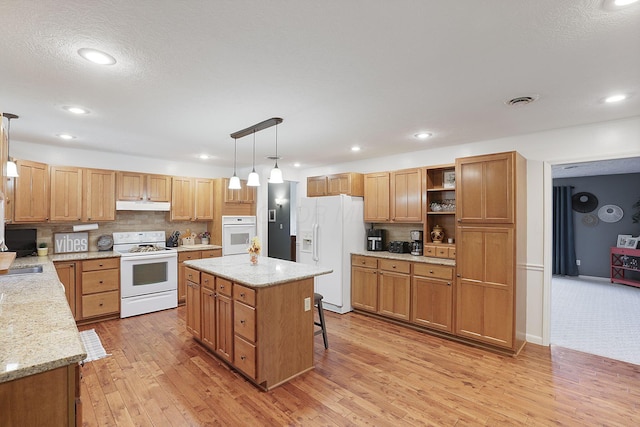 kitchen featuring white appliances, hanging light fixtures, light wood-type flooring, a center island, and backsplash