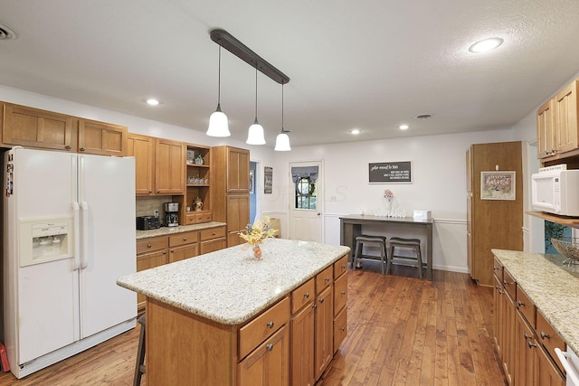 kitchen with white appliances, pendant lighting, a center island, tasteful backsplash, and hardwood / wood-style floors