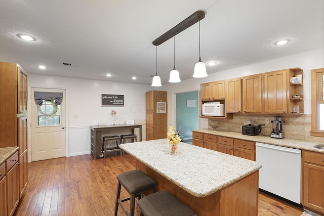 kitchen with white appliances, pendant lighting, a breakfast bar, a kitchen island, and backsplash