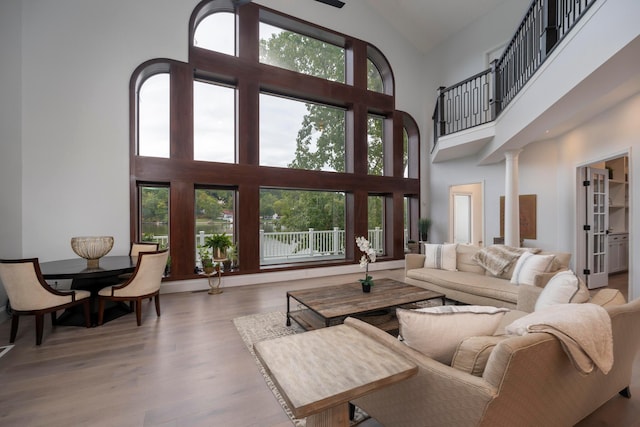 living room with hardwood / wood-style floors, plenty of natural light, high vaulted ceiling, and decorative columns