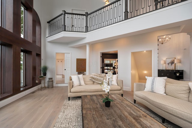 living room with a towering ceiling, light hardwood / wood-style floors, ornate columns, and a notable chandelier