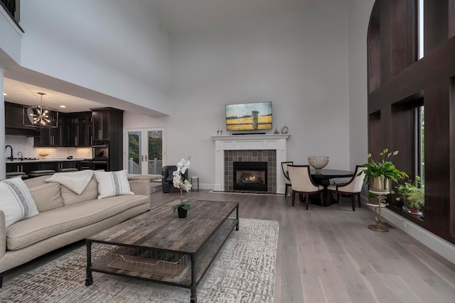 living room with sink, hardwood / wood-style floors, a towering ceiling, a chandelier, and a fireplace