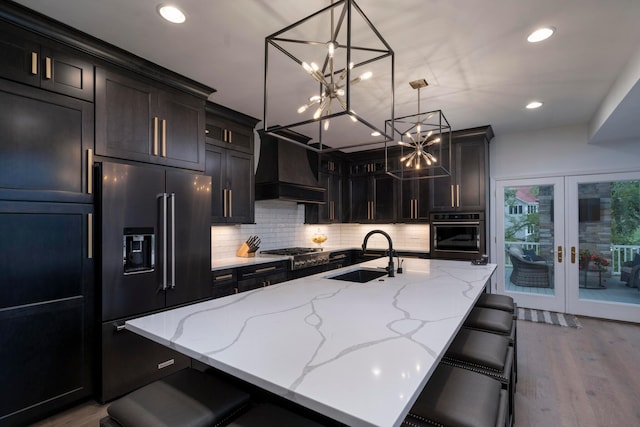 kitchen featuring premium range hood, a kitchen island with sink, sink, and appliances with stainless steel finishes