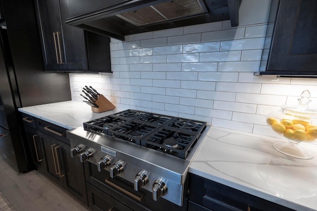 kitchen featuring light hardwood / wood-style flooring, light stone countertops, stainless steel gas cooktop, tasteful backsplash, and extractor fan