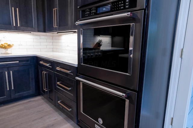 kitchen featuring double oven, decorative backsplash, light stone counters, and light hardwood / wood-style floors