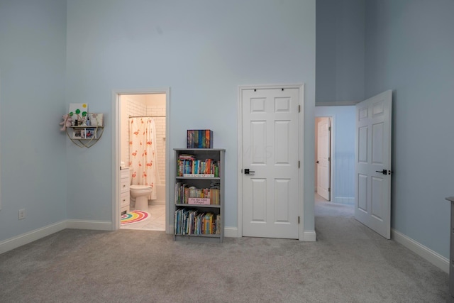 unfurnished bedroom with ensuite bath, light colored carpet, and a high ceiling