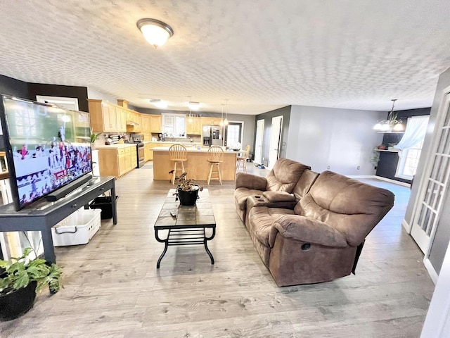 living room with light hardwood / wood-style floors, a textured ceiling, and an inviting chandelier