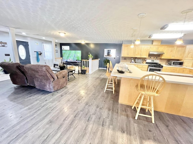 kitchen with hanging light fixtures, stainless steel appliances, light hardwood / wood-style flooring, light brown cabinetry, and a breakfast bar