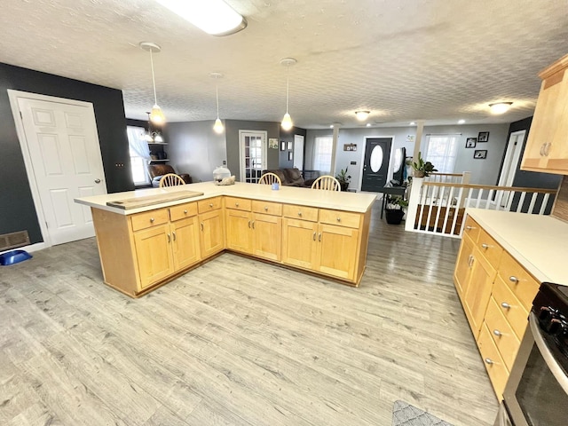 kitchen with stainless steel range, light brown cabinets, light hardwood / wood-style floors, and hanging light fixtures