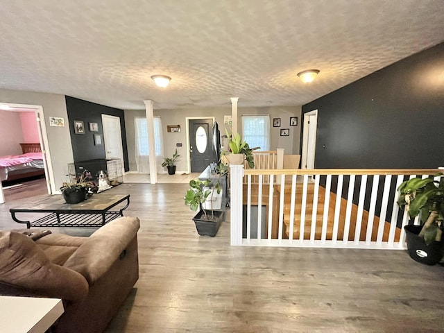 living room with wood-type flooring, a textured ceiling, ornate columns, and a healthy amount of sunlight