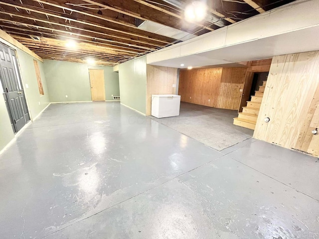 basement featuring wood walls and white refrigerator