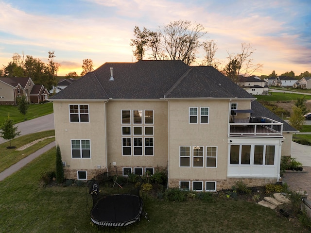 back house at dusk with a yard and a balcony