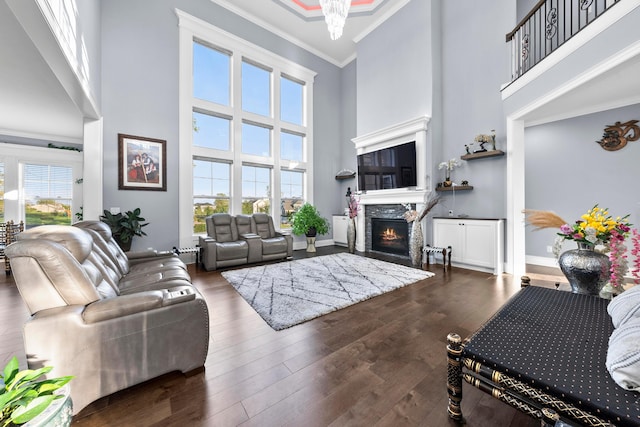 living room featuring a stone fireplace, crown molding, dark hardwood / wood-style floors, a towering ceiling, and a chandelier