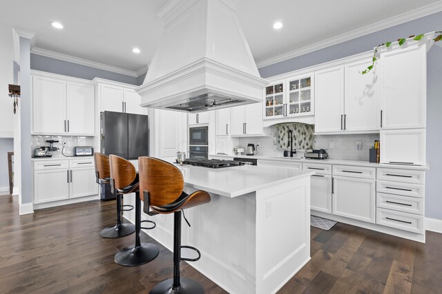 kitchen with dark hardwood / wood-style floors, an island with sink, white cabinets, black appliances, and custom range hood