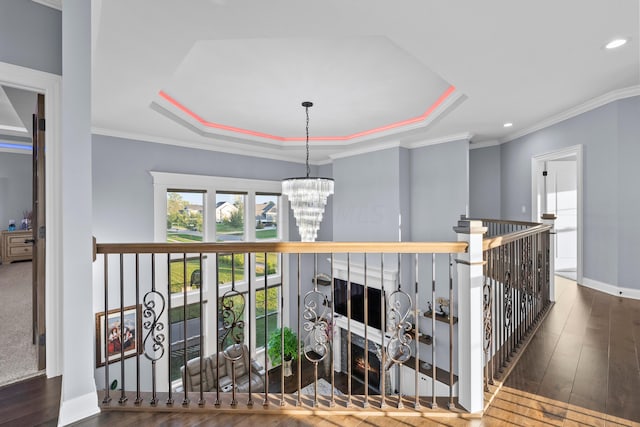 hall with a raised ceiling, crown molding, dark wood-type flooring, and an inviting chandelier