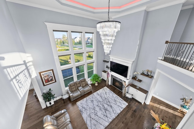 living room with dark hardwood / wood-style floors, a raised ceiling, crown molding, and a notable chandelier