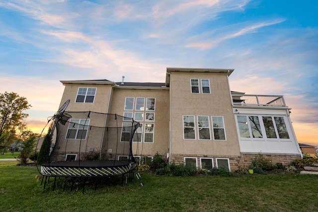 back house at dusk featuring a yard, a balcony, and a trampoline