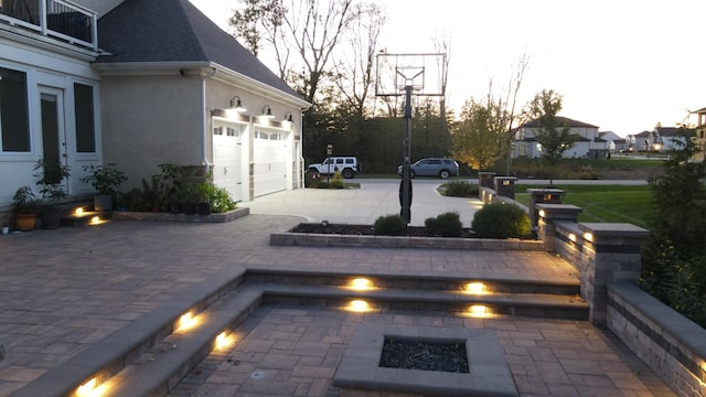 patio terrace at dusk featuring a balcony and a garage