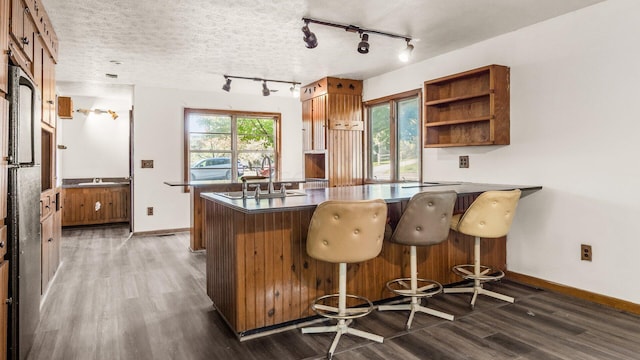 kitchen featuring sink, dark hardwood / wood-style floors, kitchen peninsula, a textured ceiling, and a kitchen bar