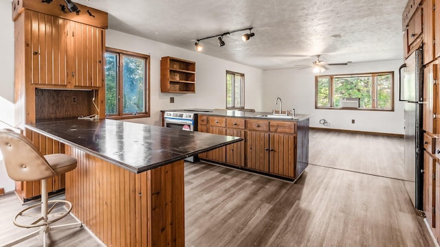 kitchen with a breakfast bar area, kitchen peninsula, ceiling fan, and dark wood-type flooring