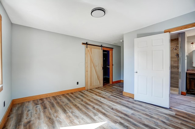 unfurnished bedroom featuring a barn door, light hardwood / wood-style floors, and connected bathroom