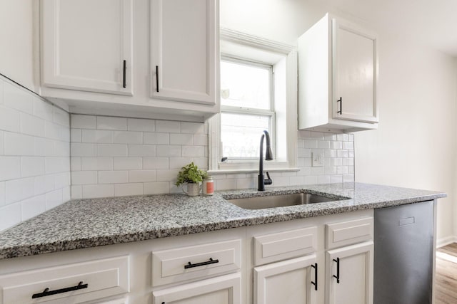 kitchen with white cabinetry, light stone countertops, and sink